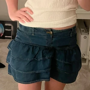 Mörkblå jeanskjol med volanger - Supersöt mörkblå jeanskjol med tre volanglager och klassiska jeansdetaljer som bälteshällor och knapp framtill. Kjolen har en kort passform och är helt perfekt till sommaren💞säljer eftersom den inte kommer till användning! Skriv prov för frågor💕