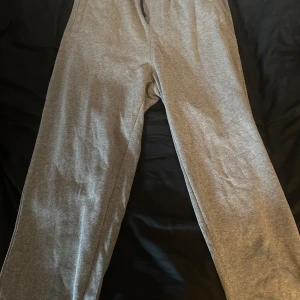 Grå mjukisbyxor i bomull - Säljer ett par klassiska grå mjukisbyxor i mjukt bomullsmaterial. De har en enkel och avslappnad passform med resår i midjan och raka ben. Perfekta för chill dagar eller när du vill vara extra bekväm.