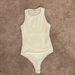 Vit ärmlös bodysuit från H&M - Säljer en stilren vit bodysuit från H&M i storlek S. Modellen är ärmlös med rund halsringning och har en tight passform. Det är dubbla tyger på framsidan och lätt att sätta ihop och ta isär nertill. Använd en gång som underplagg men passade inte mig. 