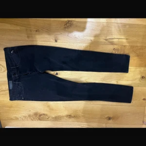 Replay Anbass jeans - Snygga svarta jeans från Replay med klassisk femficksdesign och diskret logga på fickan. Jeansen har en slim passform och raka ben, tillverkade i stretchigt jeanstyg för extra komfort. Perfekta för dig som gillar stilrena och tidlösa byxor.