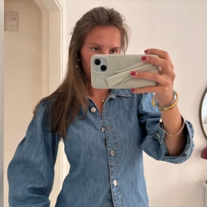 Jeansskjorta från George med puffärm - Snygg jeansskjorta från George i ljusblå denim. Skjortan har puffiga ärmar, klassisk krage och knäppning framtill med silvriga knappar. Perfekt att styla öppen eller stängd för en cool look. 