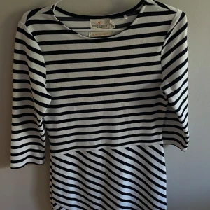 Randig klänning från Holly & White - Snygg kortklänning från Holly & White med svartvita horisontella ränder och trekvartsärm. Klänningen har en klassisk rak passform och är gjord i mjuk bomull, perfekt för en stilren look.