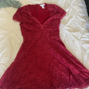 Röd klänning  - Supersöt röd kortklänning från NLY One med v-ringning och spetsdetaljer över hela klänningen. Den har korta ärmar, markerad midja och dragkedja i ryggen. Perfekt för dig som vill sticka ut med en romantisk look.