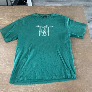 Grön t-shirt med tryck från H&M - Snygg grön t-shirt från H&M i relaxed fit med coolt tryck både fram och bak. Motivet har texten 'New Times Ancient Wisdom' och grafiska detaljer i vitt och rosa. Perfekt för dig som gillar streetstyle och unika prints.