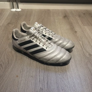 Adidas Copa Icon silver fotbollsskor - Snygga Adidas Copa Icon fotbollsskor i silver med svarta ränder och gulddetaljer på hälen. Skorna har klassisk snörning och är tillverkade i skinn för bästa känsla på planen. Perfekta för dig som vill sticka ut med stilren design och grym komfort. Skriv till mig om fler bilder. Ingen sula i skorna. Säljer dom för att skorna inte passar mig längre. 