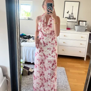 Vit långklänning med rosa blommor och halterneck - Säljer denna underbara långklänning i vitt med rosa blommigt mönster. Klänningen har halterneck med draperad urringning och knyt i nacken, samt öppen rygg. Tunt, flowy material som ger en luftig känsla. Perfekt för sommarens alla tillfällen. Den är helt oanvänd med prislapp kvar! Kan mötas upp i Stockholm city 💕 annars står köparen för frakten 💕