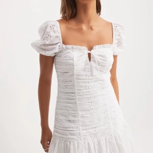 Vit kort klänning med puffärm - Superfin vit kort klänning med broderade blommor, puffiga korta ärmar och söt knytning framtill. Klänningen har volang nertill och är gjord i bomull, perfekt för sommarens alla tillfällen. Den har en romantisk och trendig look som verkligen sticker ut. Köptes till midsommar men den passade inte så den har prislapparn kvar❤️nypris 599