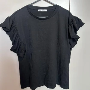 Svart volangtopp från Zara - Svart topp från Zara med volangdetaljer. Den har en liten fläck på bakre volangen men det är inget man tänker på!! Annars mycket bra skick💕💕