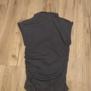  Gina Tricot soft touch - Snygg grå blå topp från Gina Tricot i storlek XS. Toppen är ärmlös med hög hals och har rynkade sidor som ger en cool och figurnära passform. 