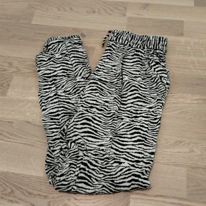 Zebramönstrade mjukisbyxor med snörning - Säljer ett par svarta och vita mjukisbyxor med zebramönster. Byxorna har resår och snörning i midjan för skön passform och är tillverkade i ett mjukt material. Perfekta för chill dagar eller när du vill sticka ut lite extra.