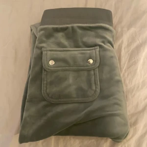 Gröna mjukisbyxor juciy  - Snygga gröna mjukisbyxor med bred resår i midjan och snörning. Byxorna har praktiska fickor med knappar och en broderad logga på sidan. Perfekta för en avslappnad stil.