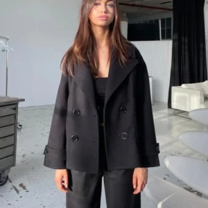 Svart kappa med knappar - Snygg svart kappa med dubbelknäppning och breda slag. Jackan har en klassisk design med långa ärmar och en lös passform. Perfekt för en stilren look. Enda defekten är att den saknar en knapp vid ärmarna annars är den som ny