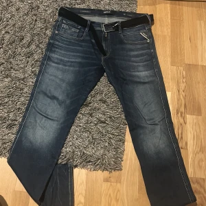 Blå jeansbyxor från Replay anbass hyperflex  - Snygga blå jeansbyxor från Replay med en klassisk femficksdesign och en bekväm passform. Byxorna har en mörk tvätt och är utrustade med en dragkedja och knappar. Perfekta för en avslappnad stil.