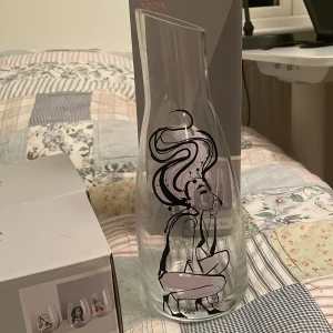 Karaff med illustration av Sara Woodrow - Elegant karaff i klart kristallglas med en unik illustration av Sara Woodrow. Rymmer 100 cl och har en modern, stilren form. Perfekt för att servera vatten eller andra drycker med stil. Designad i Sverige. Ny pris 749