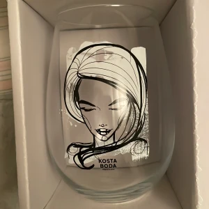 Kosta Boda glas All About You - Säljer ett set med två stilrena glas från Kosta Boda, modell All About You. Glasen rymmer 57 cl och har en elegant illustration av ett ansikte i svart. Perfekta för att ge en personlig touch till dukningen. Ny pris 499kr