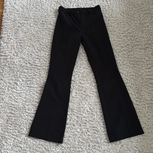 Svarta kostymbyxor - Snygga svarta bootcut kostymbyxor. Byxorna har en knapp och dragkedja framtill samt hällor för bälte. Perfekta för en stilren look. Använda en gång.