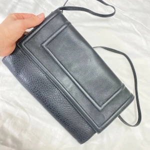 Svart axelväska i skinn - Snygg svart axelväska i skinn med enkel design och lång rem. Perfekt för att bära med sig det nödvändigaste. Stilren och lätt att matcha med olika outfits.