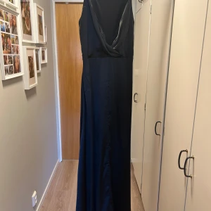 Balklänning , Svart långklänning i satin - Elegant svart långklänning i satin med en djup v-ringad rygg och smala axelband. Klänningen har en hög slits framtill som ger en sofistikerad touch. Perfekt för speciella tillfällen.  Djur och rökfritt hem, använd endast vid ett tillfälle. 