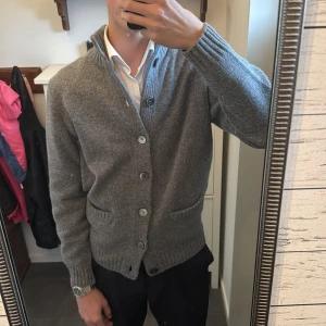 Grå kofta/Cardigan från Alan Paine - Säljer en stilren grå kofta från Alan Paine i 100% lammull. Koftan har knappar framtill och två praktiska fickor. Perfekt för kyligare dagar med sin mjuka och varma känsla. Passar både till vardag och mer uppklädda tillfällen. Helt ny kommer med tags. 