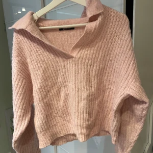 Rosa stickad tröja från Gina Tricot - Mysig rosa stickad tröja från Gina Tricot med en bred krage och ribbad struktur. Perfekt för kyliga dagar och ger en avslappnad stil. Tröjan har långa ärmar och en bekväm passform. Nypris 299kr 