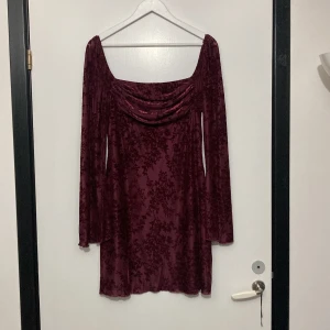 Vinröd klänning från Cider - Säljer en elegant vinröd klänning från Cider med ett vackert blommigt mönster. Klänningen har långa ärmar och en draperad halslinje som ger en stilfull look. Perfekt för speciella tillfällen eller en utekväll. Materialet är en blandning av polyester och spandex för en bekväm passform.