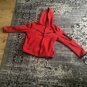 Röd hoodie från Nike - Köpte den i Nike festival förra sommaren för 1800 den är limited e edition Ajax Nike tech Säljer en snygg röd hoodie från Nike med dragkedja och huva. Jackan har svarta detaljer och en praktisk ficka med dragkedja på ärmen. Perfekt för en sportig look!