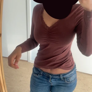 Brun/röd  långärmad topp - Säljer en snygg brun långärmad topp med v-ringning och rynkdetalj framtill. Perfekt för en stilren look. Passar bra till jeans eller kjol.