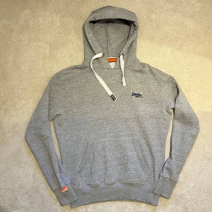 Superdry - Grå Hoodie  - Säljer en stilren grå hoodie från Superdry med broderad logga på bröstet. Riktig snygg och eftertraktad. Vid minsta fråga eller fundering hör av er🤝