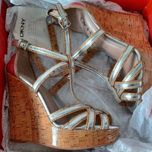  DKNY Kilklackar - OANVÄNDA! - Snyggaste skorna i sommar till KANON pris. Helt oanvända DKNY kilklackar inköpta på DKNY - Bondstreet i London.                                                  Remmar i ljusbrunt läder med silver samt lackad korksula. Storlek 37 (6.5)                               Nypris ca £200                                                       PM för mer info/bilder. FÖRST TILL KVARN...                                         .                                                                      