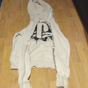 Beige hoodie med PlayStation-tryck - Säljer en beige hoodie med PlayStation-tryck. Den har en stor logga på framsidan och text längs ärmarna. Perfekt för gamingkvällar eller som en casual vardagströja. Storleken är 170
