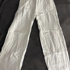 Vita linnebyxor från Lindex - Säljer ett par vita linnebyxor från Lindex i storlek 146. Byxorna har en elastisk midja och är tillverkade i ett lätt och luftigt material, perfekt för varma dagar. De har en avslappnad passform och sidofickor för extra bekvämlighet.