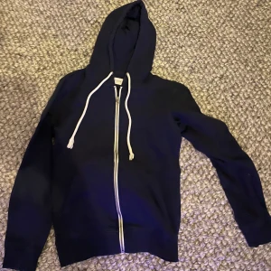 Mörk blå hoodie från Pier One - Säljer en stilren mörk blå hoodie från Pier One med dragkedja och justerbar huva. Perfekt för en avslappnad look. Den har långa ärmar och en bekväm passform. Modellen är 180.