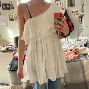 Vit offshoulder klänning med volang - Vit offshoulder klänning med volangdetaljer. Klänningen har en luftig och flödande design med plisserade detaljer som ger en elegant touch. Helt oanvänd men köpt tidigare på Plick. Väldigt bra skick. Inget tag. 