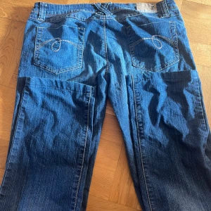 Blå jeans från Urban Heart - Snygga blå jeans från Urban Heart med coola detaljer på bakfickorna. De har en klassisk femficksdesign och en knapp med märkets logga. Perfekta för en avslappnad stil.