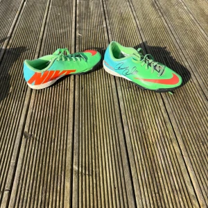 Gröna fotbollsskor från Nike med Thomas ravelli autograf  - Säljer ett par gröna fotbollsskor från Nike med röda och blå detaljer. Skorna har snörning och en sportig design, perfekt för fotbollsplanen. Stora Nike-loggor på sidorna ger en cool look. Grus eller konstgräs skor.