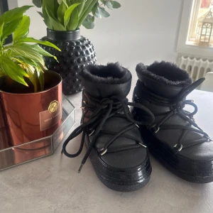 Svarta boots från Inuikii - Säljer ett par svarta boots från Inuikii med snörning och fluffigt foder. Perfekta för kalla dagar med sin robusta sula och stilrena design. De är gjorda i skinn och har en mysig insida som håller fötterna varma.