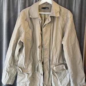 Beige jacka från Conwell - Säljer en stilren beige rock/jacka från Conwell. Jackan har en klassisk krage och knäppning framtill. Perfekt för vår och höst. Den har praktiska fickor och en avslappnad passform. Defekter syns i sista bilden, två hål på jackans baksida.⭐️🧥