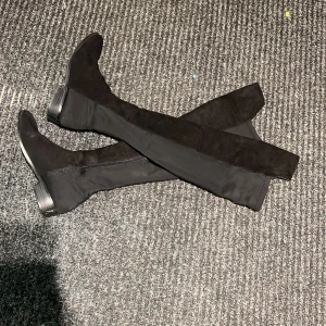Svarta overknee stövlar med dragkedja - Snygga svarta overknee stövlar i mocka med dragkedja på sidan. Perfekta för en stilren look och passar bra till både kjol och jeans. De har en låg klack och en spetsig tå som ger en elegant touch.