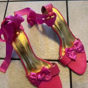 Rosa klackskor med rosett från Soever - Snygga rosa klackskor från Soever med en elegant rosett på framsidan och knytband runt ankeln. Perfekta för att sätta färg på din outfit. Se bilder för skick