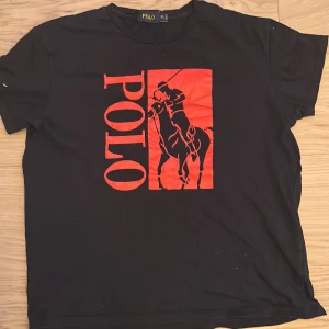 Svart t-shirt från Polo - Säljer en svart t-shirt från Polo med ett stort rött tryck av en häst och ryttare på framsidan. T-shirten är tillverkad i 100% bomull och har korta ärmar. Perfekt för en avslappnad stil. Den är äkta och säljer den för att jag ränslar kläder som är för små. Den är XL i bran storlek och är då en S/M
