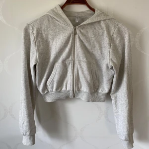 Grå hoodie från H&M Divided - Säljer en grå hoodie från H&M Divided. Den har en dragkedja framtill och en mysig huva. Tröjan är croppad och har långa ärmar med ribbade muddar. Perfekt för en avslappnad stil! 🩶