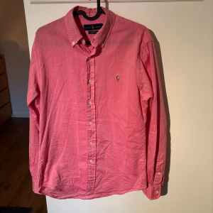 Rosa skjorta från Ralph Lauren - Snygg rosa skjorta från Ralph Lauren i slim fit. Skjortan har långa ärmar och knappar framtill. Perfekt för en stilren look med klassisk design och broderad logga på bröstet.