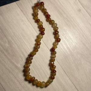 Halsband med bruna och gula pärlor - Snyggt halsband med pärlor i olika nyanser av brunt och gult. Perfekt för att ge en naturlig touch till din outfit. Pärlorna är jämnt fördelade och ger en fin glans.