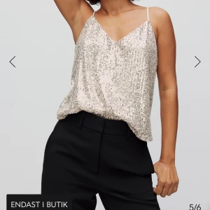 Glittrig linne i silver - Säljer en snygg glittrig linne i silver med smala axelband och v-ringning. Perfekt för en kväll ute eller festliga tillfällen. Lätt att matcha med både kjol och byxor för en stilren look.