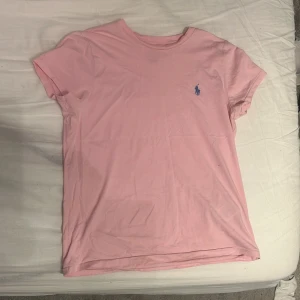 Rosa t-shirt från Ralph Lauren - Säljer en snygg rosa t-shirt från Ralph Lauren med den snygga blåa Ralph lauren logan på bröstet. T-shirten är kortärmad och tillverkad i mjuk bomull. Perfekt för en avslappnad stil. |storlek S| Nypris: 799kr 
