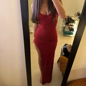 Balklänning - Elegant vinröd axelbandslös klänning med draperad design och hög slits. Klänningen har en figurnära passform som framhäver silhuetten. Materialet är i mesh och är storlek S, lappen är kvar. Säljer pga kunde inte göra retur. Köpt för 1420kr från BabyBoo. Pris kan diskuteras❤️