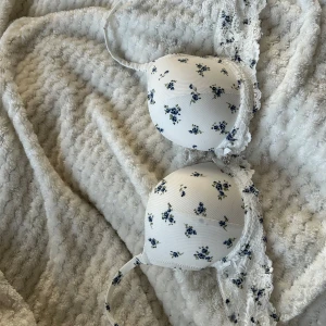 Vit med blåa blommor bh från NEW YORKER den är aldrig använd. Den har spets   - Säljer en söt vit bh med blå blommor från NEW YORKER. Den har spetsdetaljer  och en liten bloms framtill. Perfekt för en romantisk look! 💙Den är mjuk och skön och fin. priset är inte satt Är öppen för pris förslag.