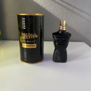 Jean Paul Gaultier Le Male Le Parfum - Säljer en elegant parfym från Jean Paul Gaultier, Le Male Le Parfum. Flaskan har en unik design i form av en svart torso med gulddetaljer. Förpackningen är en stilren svart burk med guldtext. Perfekt för den som vill ha en sofistikerad doft.