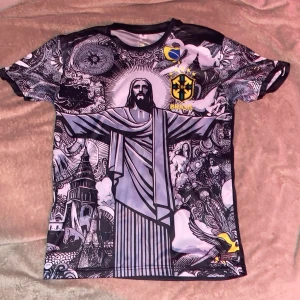 Fotbollströja med Kristusmotiv - Unik fotbollströja med ett stort Kristusmotiv på framsidan och brasiliansk symbolik. Tröjan har korta ärmar med detaljerade mönster och en mörk basfärg. Perfekt för den som vill sticka ut på planen eller visa sin kärlek för Brasilien.