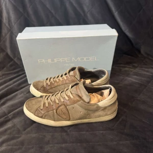 Philippe Model - FRI FRAKT! SJUKT BRA PRIS Snygga bruna sneakers från Philippe Model i mocka. Skorna har en klassisk design med snörning och en bekväm sula. Perfekta för en stilren look. Deffekterna på utsidan är inga skador.